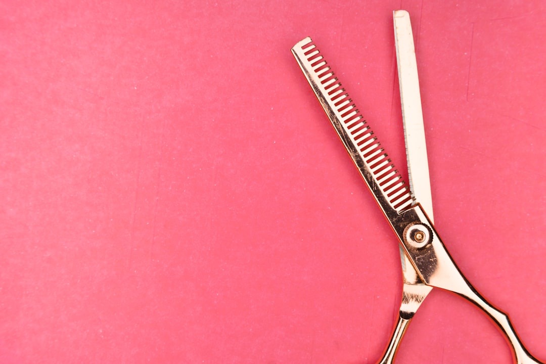 Golden thinning shears laid flat on a pink surface.