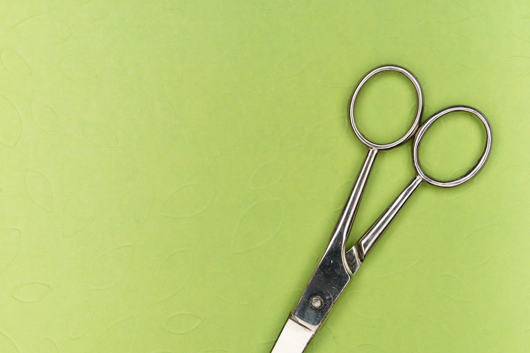 Silver scissors lie on a lime green leaf-patterned background.