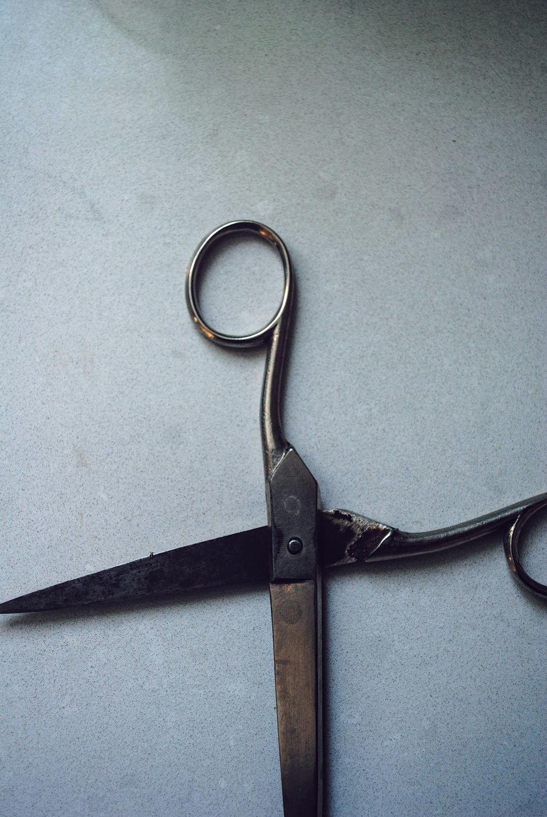 Old rusty metal scissors resting on a textured surface.